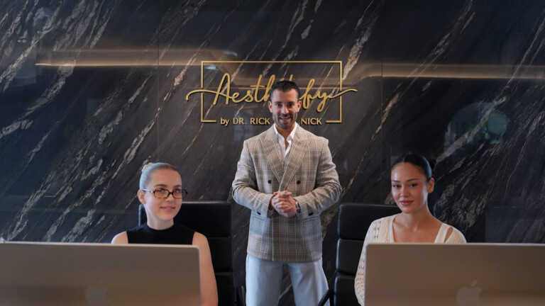 Aesthetify Düsseldorf – Mitarbeitende am Empfangstresen vor der Marmorwand mit beleuchtetem Aesthetify-Logo