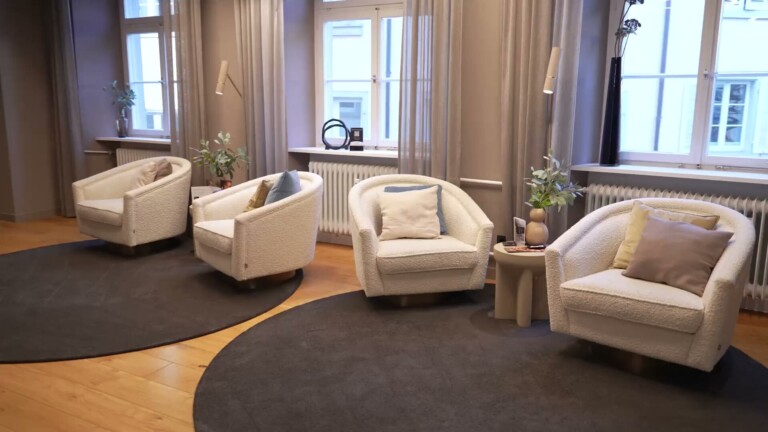Aesthetify Konstanz – Waiting area with four light armchairs and a round rug in front of period windows