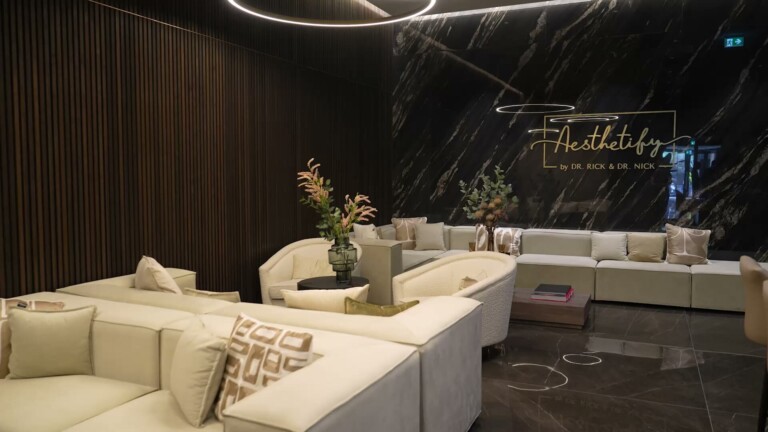 Aesthetify München – Loungebereich mit heller Sofalandschaft vor Marmorwand mit Aesthetify-Schriftzug